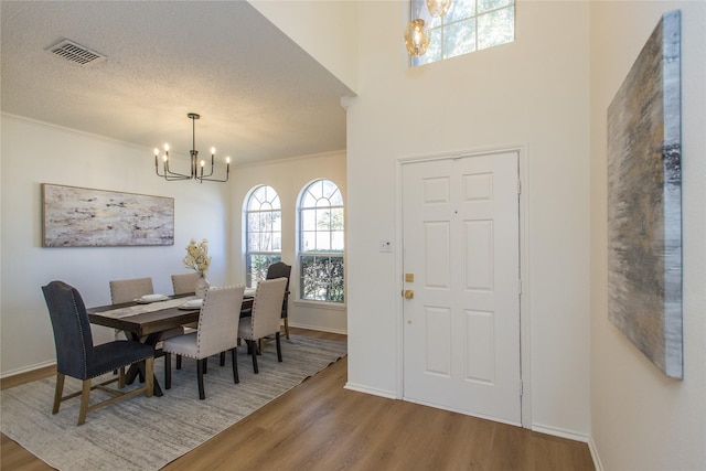 dining room featuring hardwood / wood-style flooring, crown molding, a textured ceiling, and a notable chandelier