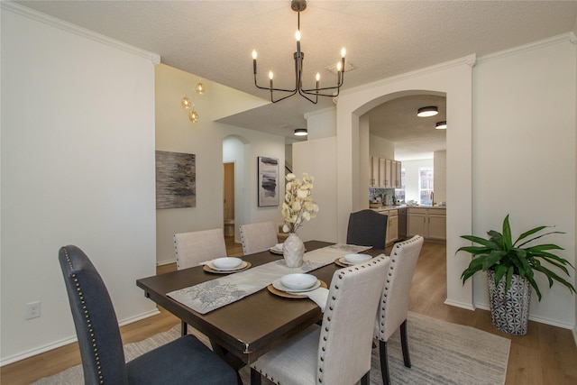 dining area featuring wood-type flooring, a textured ceiling, a notable chandelier, and crown molding