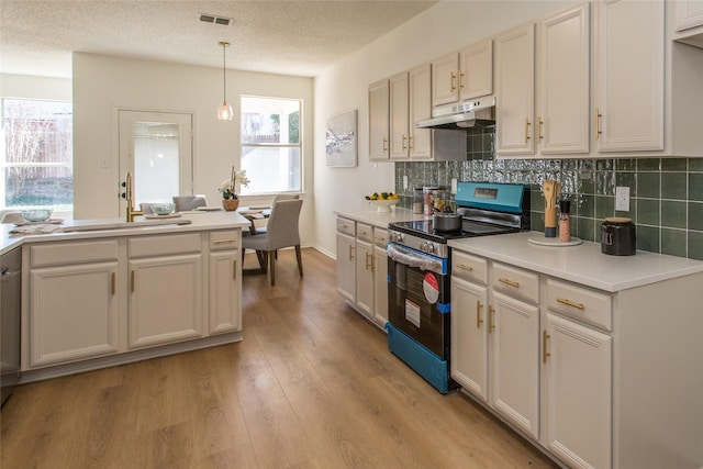 kitchen featuring stainless steel range with electric cooktop, tasteful backsplash, hanging light fixtures, a textured ceiling, and light hardwood / wood-style floors