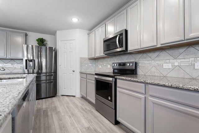 kitchen featuring sink, backsplash, light stone counters, light hardwood / wood-style floors, and stainless steel appliances