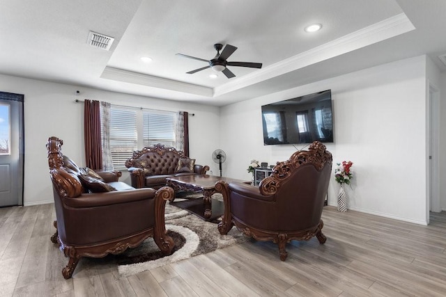 living room featuring crown molding, light hardwood / wood-style floors, a raised ceiling, and ceiling fan