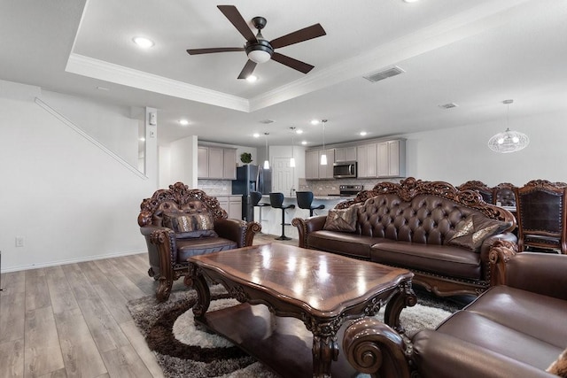 living room with crown molding, ceiling fan, light hardwood / wood-style floors, and a tray ceiling