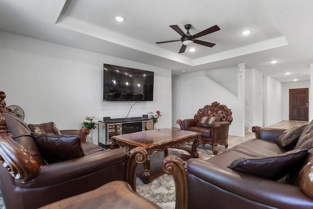 living room featuring ceiling fan, ornamental molding, and a tray ceiling