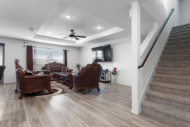 living room featuring light hardwood / wood-style flooring, a raised ceiling, and ceiling fan