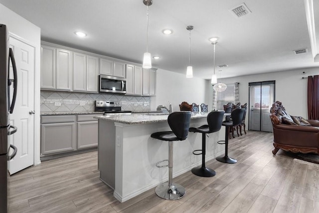 kitchen with decorative light fixtures, an island with sink, a breakfast bar area, light stone counters, and stainless steel appliances