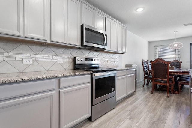 kitchen featuring hanging light fixtures, stainless steel appliances, tasteful backsplash, light stone countertops, and light hardwood / wood-style floors