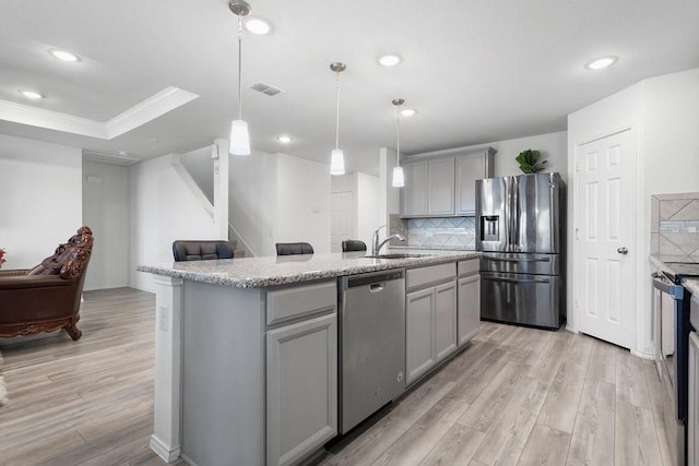 kitchen featuring an island with sink, sink, gray cabinetry, hanging light fixtures, and stainless steel appliances