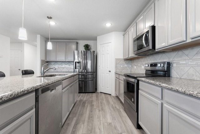 kitchen with hanging light fixtures, light hardwood / wood-style flooring, appliances with stainless steel finishes, gray cabinets, and light stone countertops