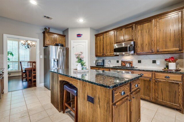 kitchen with dark stone counters, light tile patterned floors, a kitchen island, stainless steel appliances, and decorative backsplash