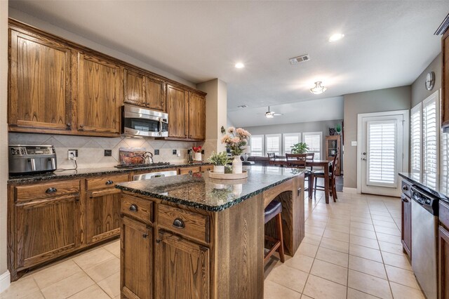 kitchen featuring dark stone counters, a wealth of natural light, a center island, and backsplash