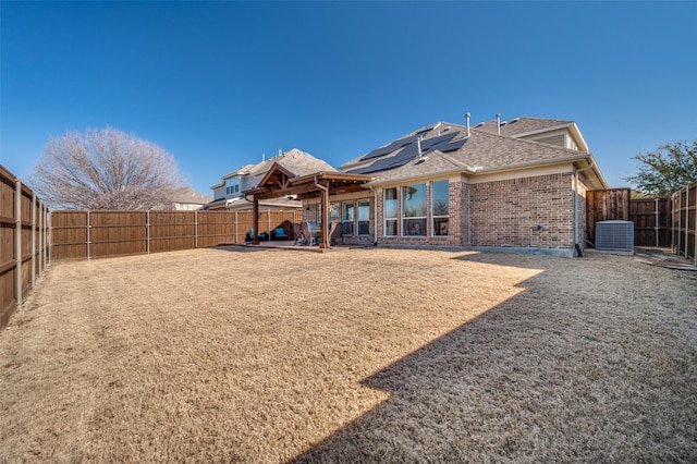 back of property with a patio, a fenced backyard, central air condition unit, brick siding, and roof mounted solar panels