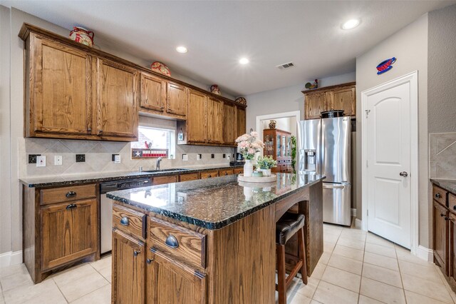 kitchen with a center island, light tile patterned floors, dark stone countertops, stainless steel appliances, and decorative backsplash