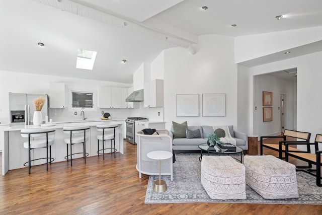 living room featuring high vaulted ceiling, a skylight, sink, dark wood-type flooring, and beam ceiling