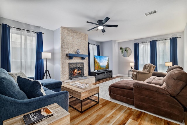 living room featuring a stone fireplace, ceiling fan, and light wood-type flooring