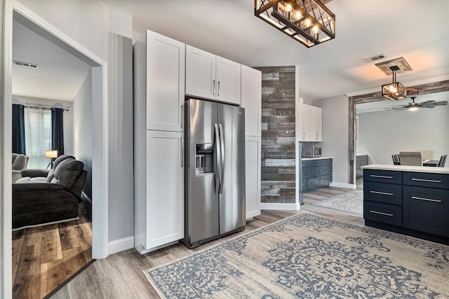 kitchen featuring stainless steel refrigerator with ice dispenser, blue cabinetry, white cabinetry, hanging light fixtures, and light wood-type flooring