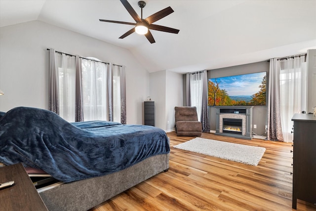 bedroom with multiple windows, vaulted ceiling, wood-type flooring, and a fireplace