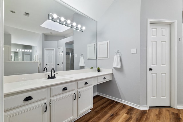 bathroom with vanity, hardwood / wood-style flooring, vaulted ceiling with skylight, and walk in shower