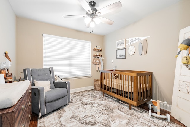 bedroom with a nursery area, ceiling fan, and hardwood / wood-style flooring