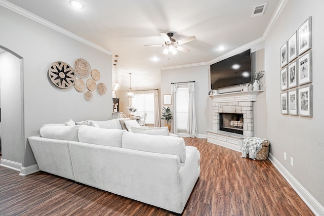 living room featuring ornamental molding, a stone fireplace, dark wood-type flooring, and ceiling fan