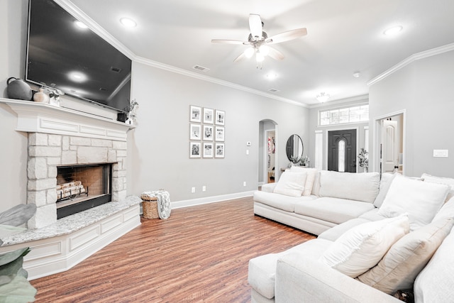 living room featuring crown molding, ceiling fan, a stone fireplace, and hardwood / wood-style floors