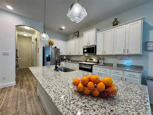 kitchen with sink, pendant lighting, stainless steel appliances, a kitchen island with sink, and white cabinets