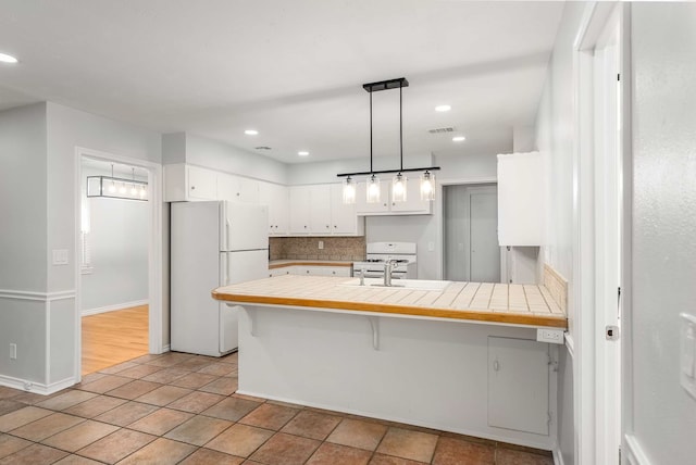 kitchen featuring tile countertops, decorative light fixtures, white cabinetry, a breakfast bar area, and white appliances