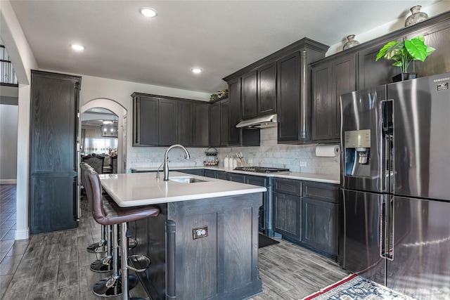 kitchen featuring arched walkways, stainless steel appliances, backsplash, a sink, and under cabinet range hood