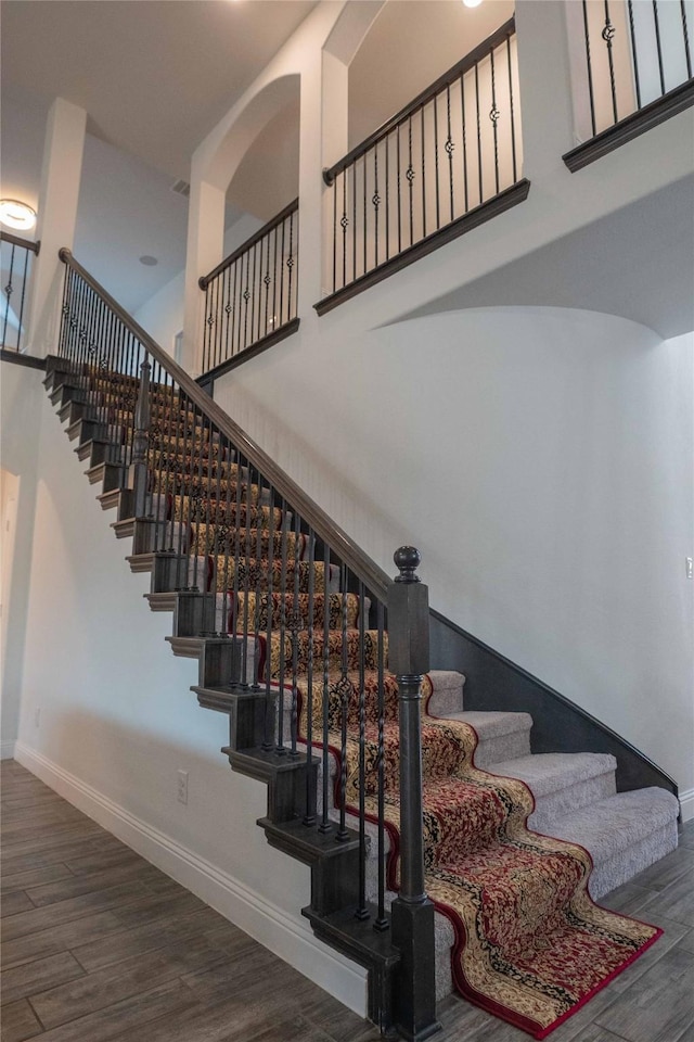 staircase featuring a high ceiling, wood finished floors, and baseboards