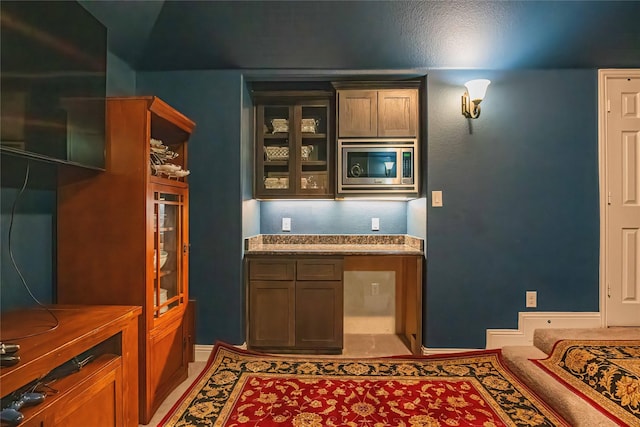 bar with built in desk, stainless steel microwave, light tile patterned flooring, and baseboards