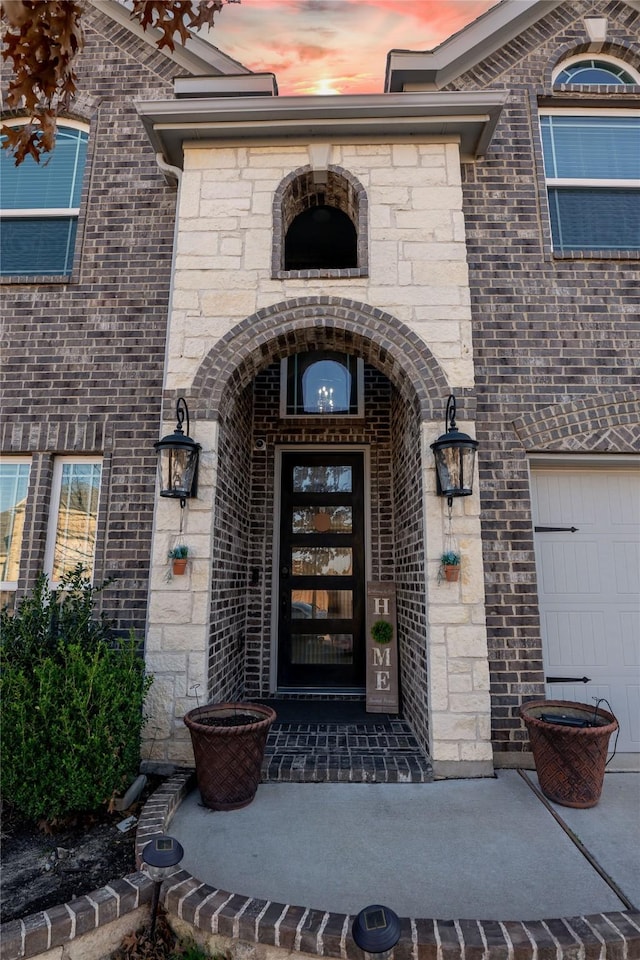 entrance to property with a garage, stone siding, and brick siding