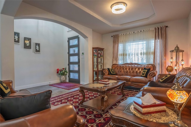 living room featuring arched walkways, a raised ceiling, baseboards, and wood finished floors