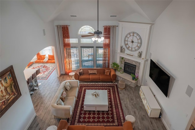 living area featuring a ceiling fan, a fireplace with raised hearth, visible vents, and wood finished floors