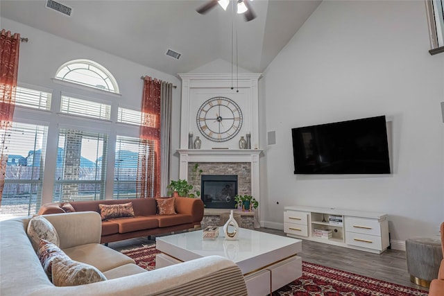 living room featuring ceiling fan, a fireplace, visible vents, and dark wood finished floors