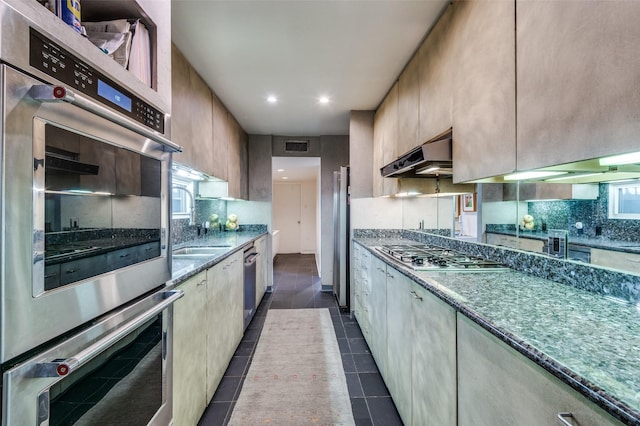 kitchen with dark tile patterned floors, dark stone countertops, backsplash, stainless steel appliances, and light brown cabinets