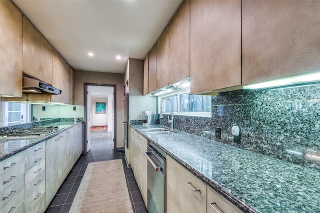 kitchen with sink, appliances with stainless steel finishes, dark tile patterned floors, dark stone counters, and backsplash