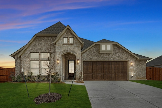 french provincial home with driveway, stone siding, an attached garage, fence, and a front yard