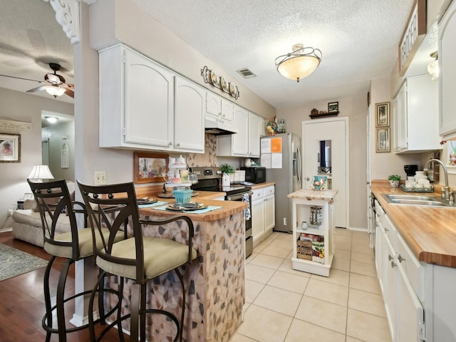 kitchen featuring sink, butcher block countertops, light tile patterned floors, stainless steel appliances, and white cabinets