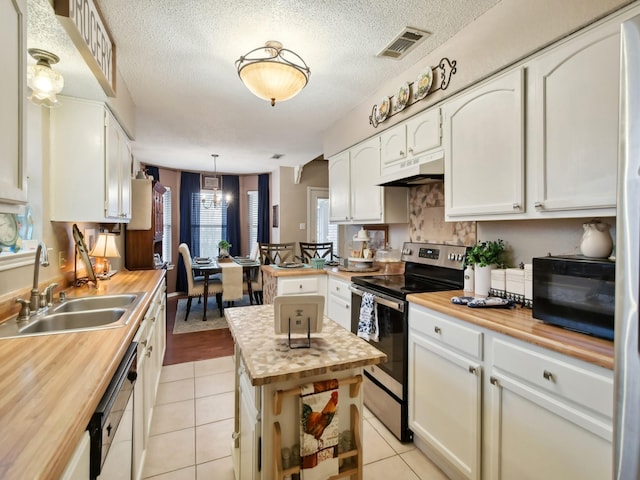 kitchen with light tile patterned floors, under cabinet range hood, butcher block counters, a sink, and stainless steel range with electric stovetop