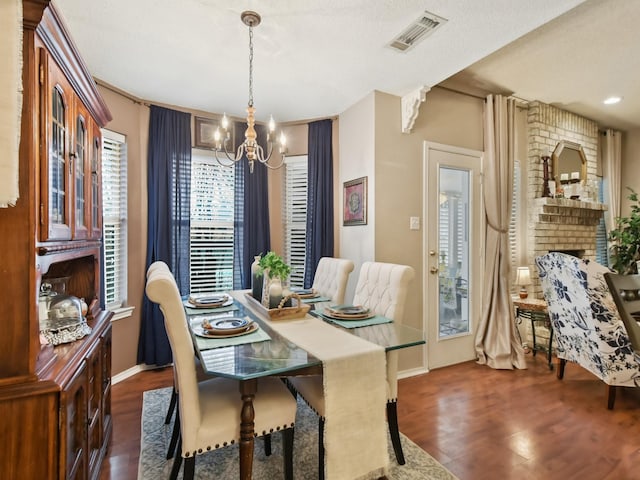 dining area with a brick fireplace, dark wood finished floors, visible vents, and an inviting chandelier