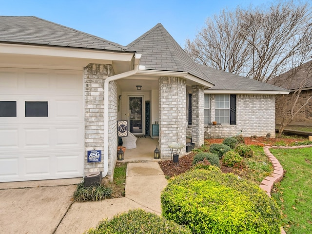 entrance to property with an attached garage, roof with shingles, and brick siding