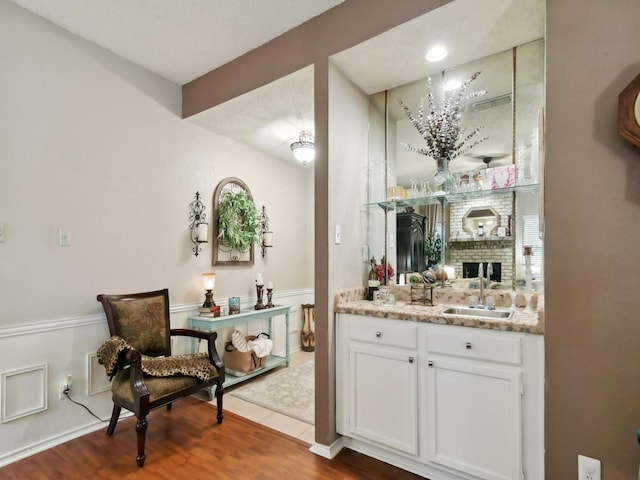 bar with sink, white cabinetry, light stone counters, a brick fireplace, and hardwood / wood-style floors