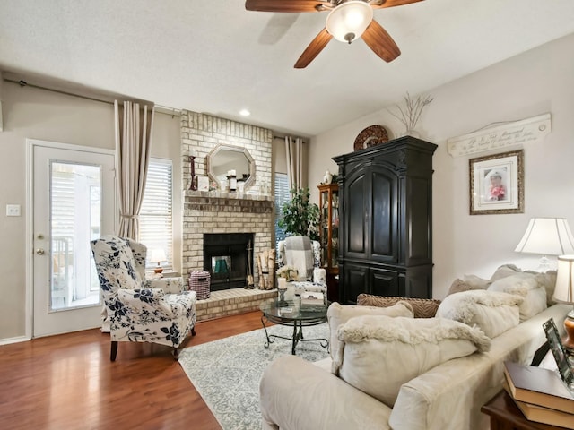 living area with a brick fireplace, ceiling fan, and wood finished floors