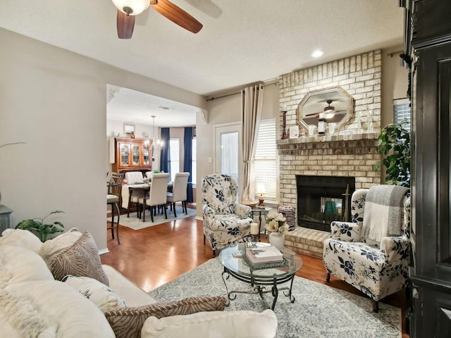 living room with a brick fireplace, hardwood / wood-style flooring, and ceiling fan with notable chandelier