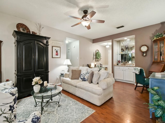 living room with a textured ceiling, wood finished floors, visible vents, and a ceiling fan