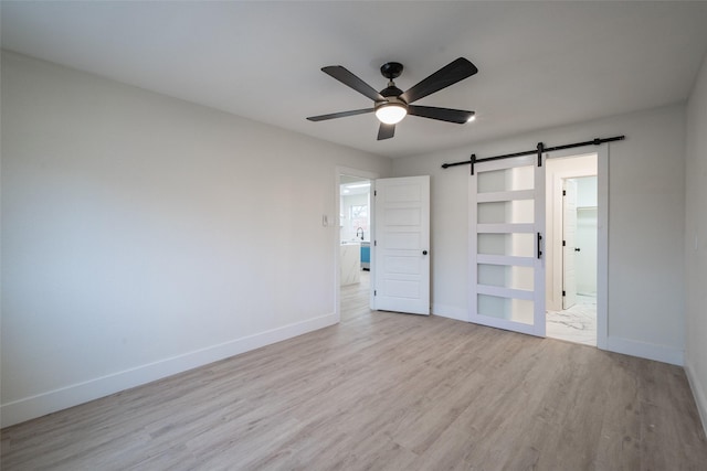 unfurnished bedroom with ensuite bathroom, a barn door, ceiling fan, and light hardwood / wood-style floors