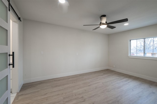 spare room featuring ceiling fan, a barn door, and light hardwood / wood-style flooring