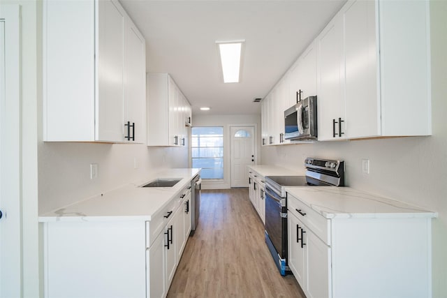 kitchen featuring sink, white cabinetry, light wood-type flooring, appliances with stainless steel finishes, and light stone countertops