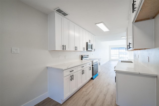 kitchen with appliances with stainless steel finishes, sink, white cabinets, light stone counters, and light hardwood / wood-style floors