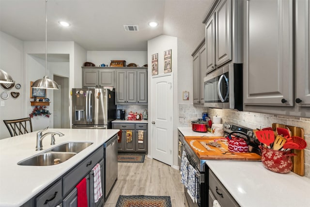 kitchen with gray cabinets, a sink, stainless steel appliances, light countertops, and light wood-style floors