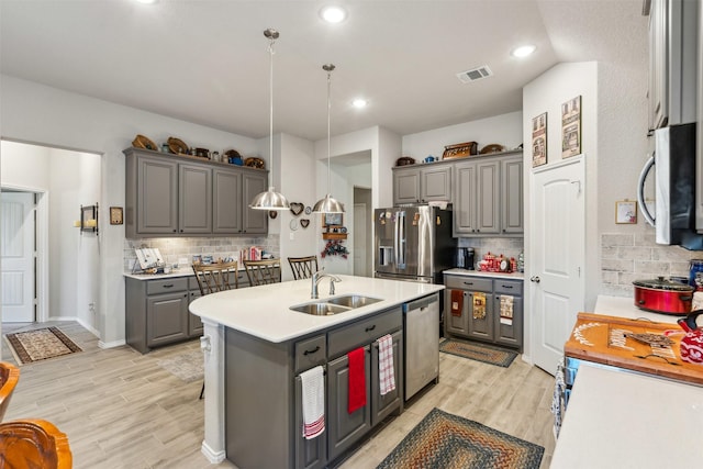 kitchen with a kitchen island with sink, gray cabinets, a sink, stainless steel appliances, and light countertops